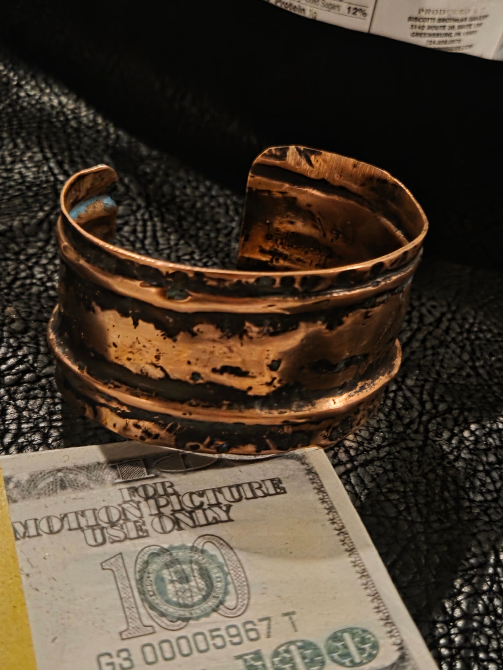 Bronze bracelet on a textured surface with a dollar bill