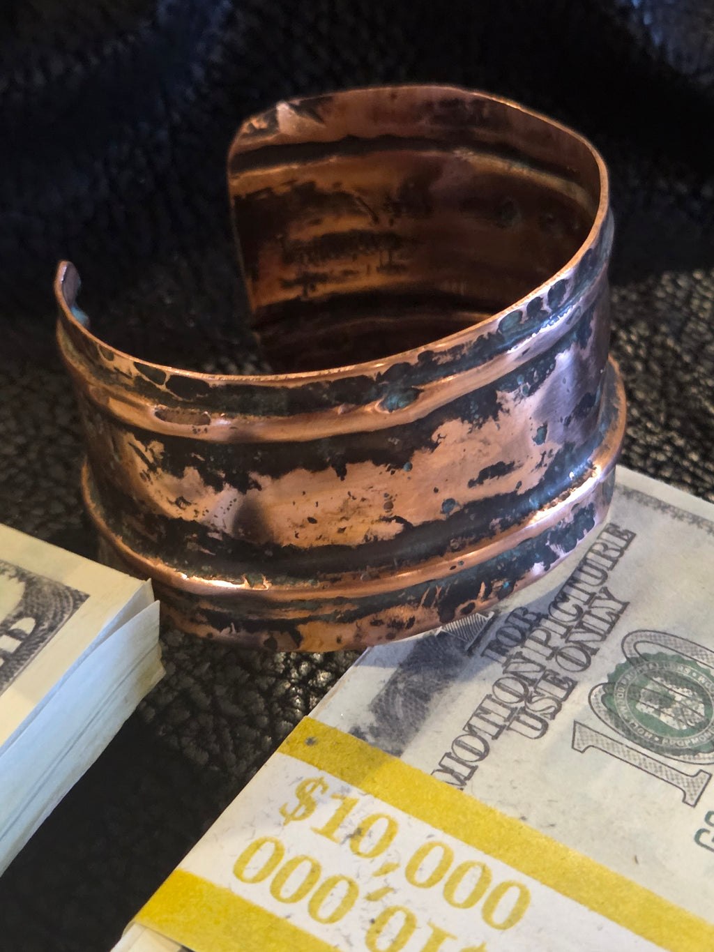 Copper bracelet on a textured surface with a $100 bill underneath