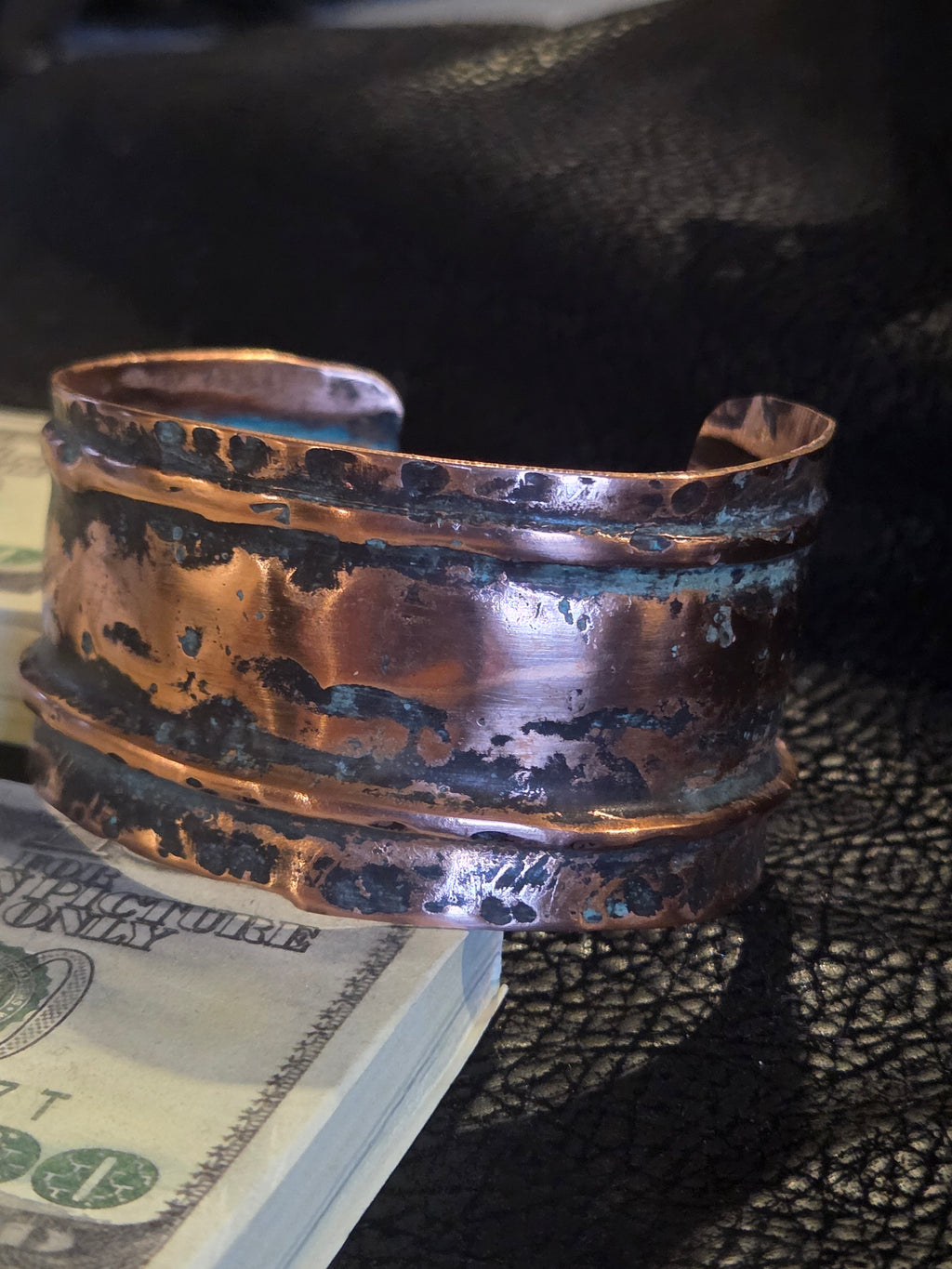 Copper-colored metal component on a textured surface with a blurred dollar bill in the background