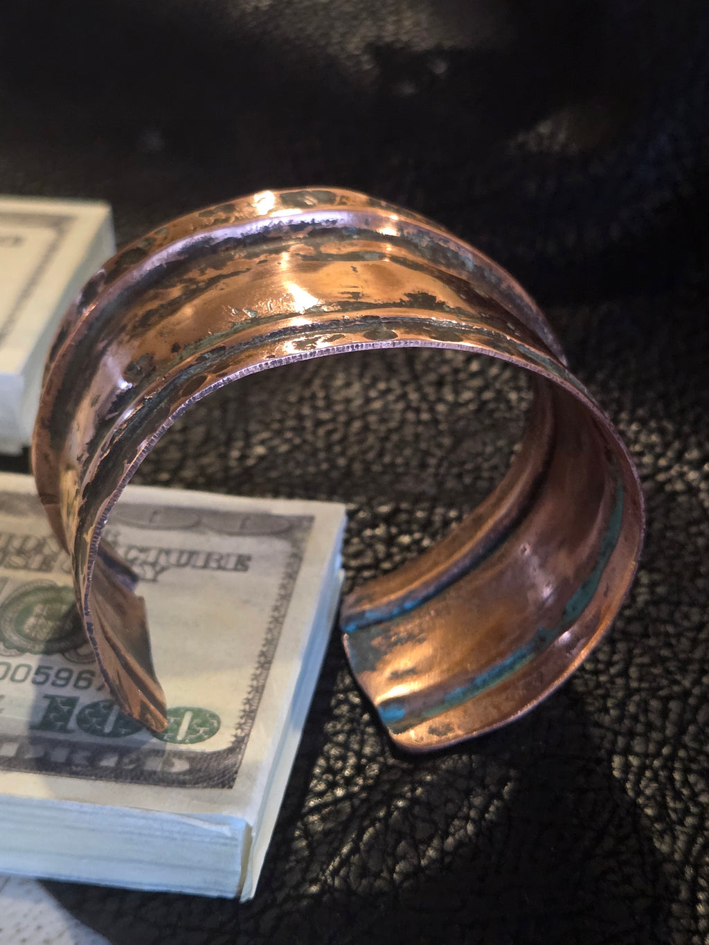 Copper ring holding a stack of dollar bills against a textured black background