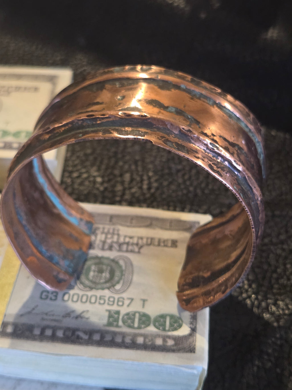 Copper bracelet holding a folded dollar bill against a dark background